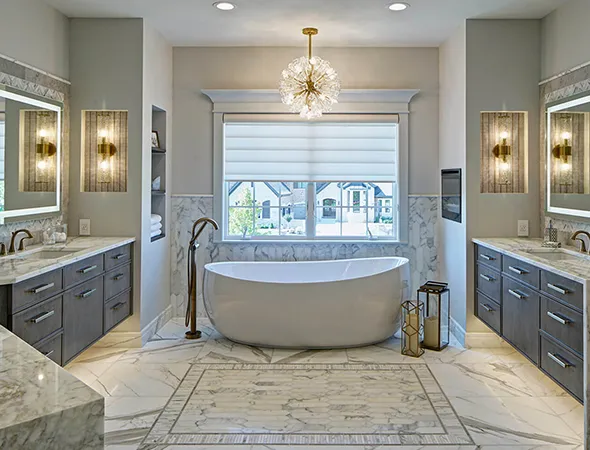Luxurious bathroom with a freestanding bathtub, elegant marble flooring, dual vanities, modern hanging lights, and a large window with blinds.