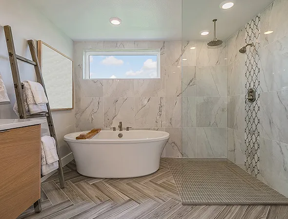 Modern bathroom with a freestanding oval bathtub beside a wooden ladder holding towels. Marble tiles and a spacious glass shower create a serene, luxurious feel.