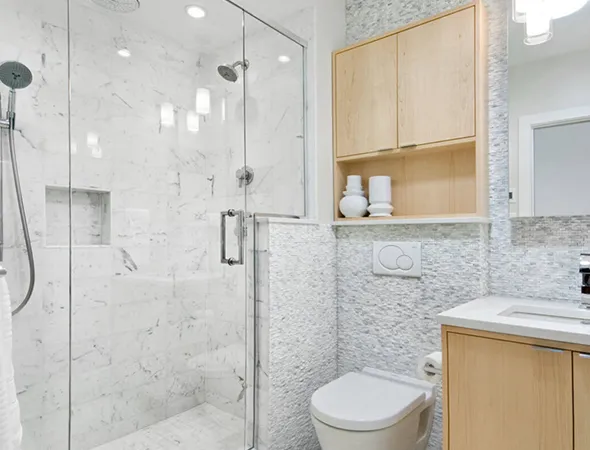 Bright modern bathroom with a glass-enclosed shower, marble tiles, light wood cabinets, and a wall-mounted toilet. The ambiance is clean and refreshing.