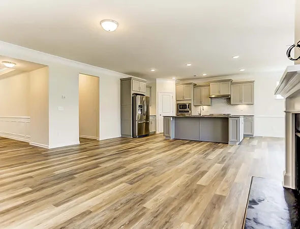 Modern open-concept kitchen and living area with wood flooring, neutral walls, and recessed lighting. Features gray cabinets and stainless steel appliances.
