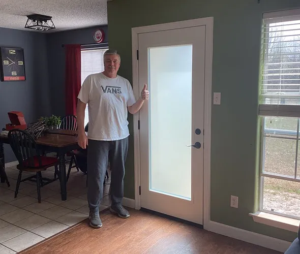 Man in Vans shirt gives thumbs up by frosted glass door in cozy room. Dining area with red accents visible. Bright, welcoming atmosphere.
