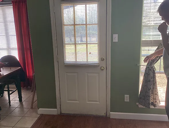 A white door with a small window, set against a green wall, flanked by two windows that create a bright and welcoming entrance.